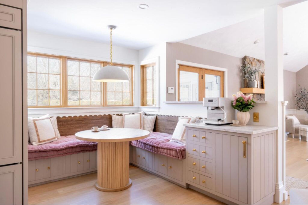 A bright kitchen nook by a custom home builder Concord features built-in bench seating, light cushions, a round table, a coffee machine on a small counter, and large windows that fill the space with natural light. A bright kitchen nook by a custom home builder Concord features built-in bench seating, light cushions, a round table, a coffee machine on a small counter, and large windows that fill the space with natural light.