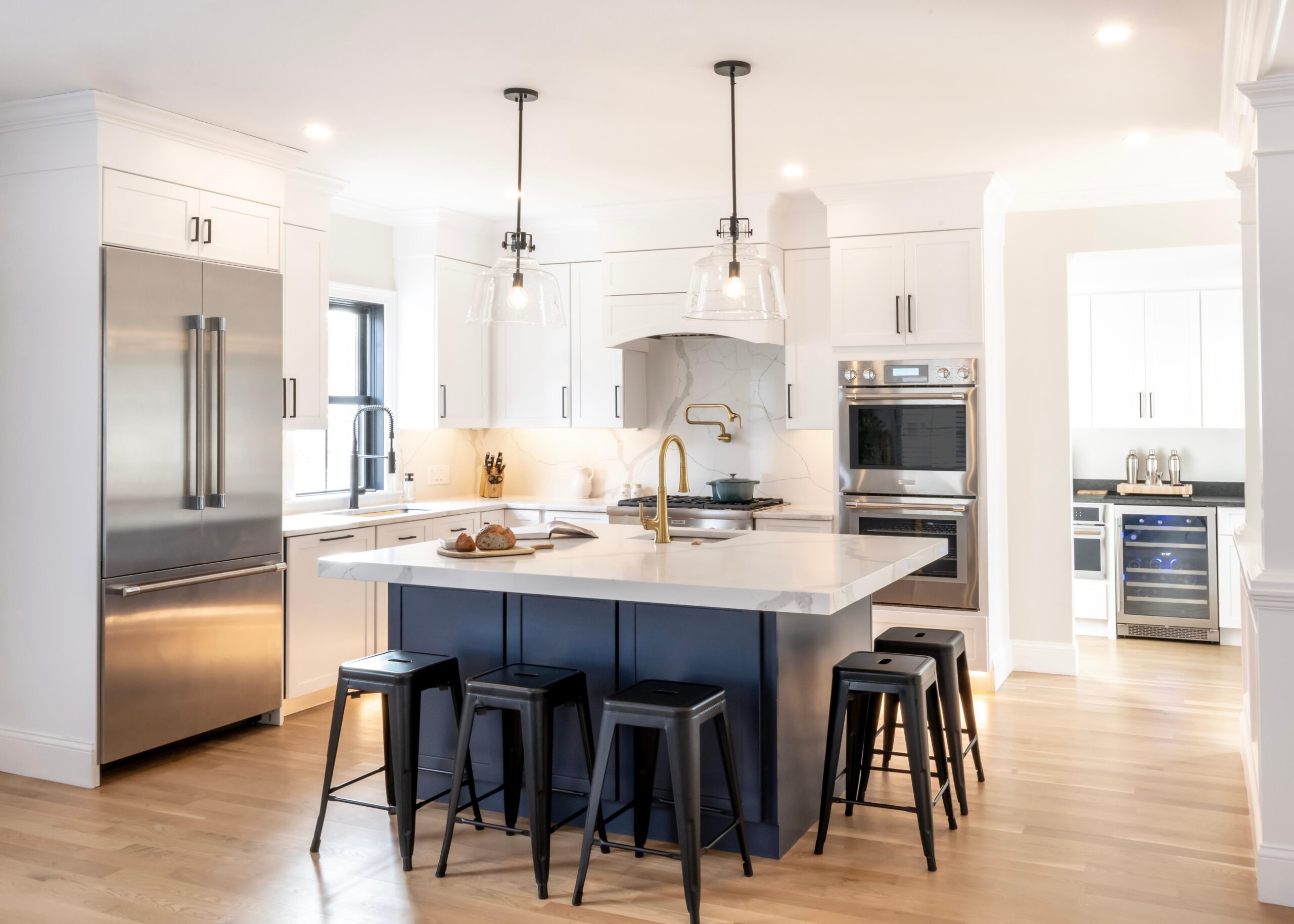 Modern kitchen with white cabinets, stainless steel appliances, a large island with bar stools, pendant lights, and light wood flooring. Modern kitchen with white cabinets, stainless steel appliances, a large island with bar stools, pendant lights, and light wood flooring.