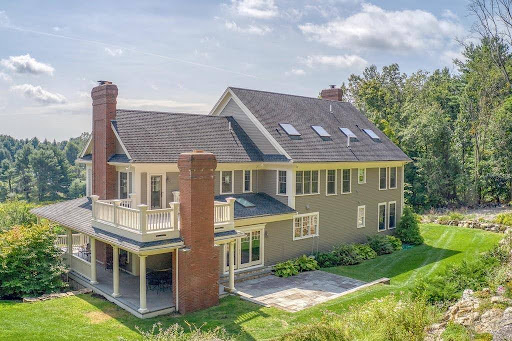 Large two-story suburban house with multiple chimneys, a covered porch, skylights, and landscaped yard—recently enhanced by an exterior home renovation MA—set against a backdrop of trees and blue sky. Large two-story suburban house with multiple chimneys, a covered porch, skylights, and landscaped yard—recently enhanced by an exterior home renovation MA—set against a backdrop of trees and blue sky.