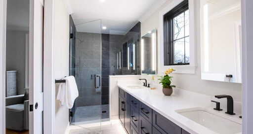 Modern bathroom with double vanity, white countertops, black fixtures, a glass-enclosed shower, and a window above the sink.