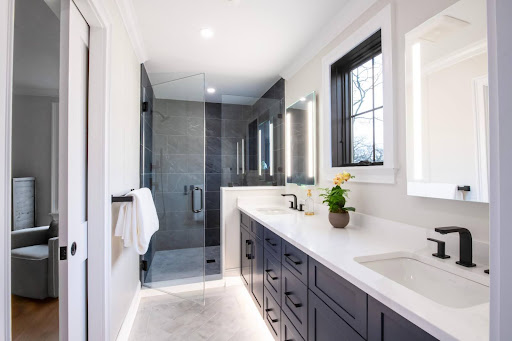 Modern bathroom with double vanity, white countertops, black fixtures, a glass-enclosed shower, and a window above the sink.