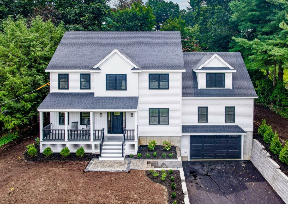 Two-story white house with black roof and attached double garage, surrounded by trees and a partially landscaped yard. Two-story white house with black roof and attached double garage, surrounded by trees and a partially landscaped yard.
