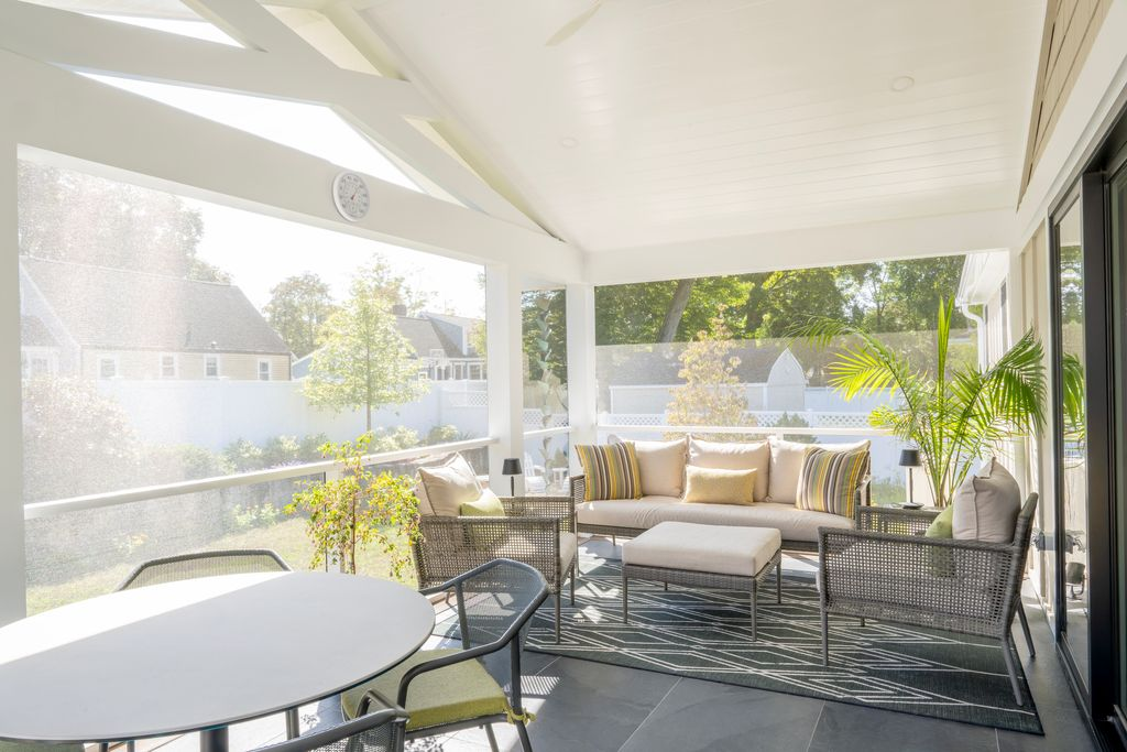 A bright, screened-in porch with cushioned seating, a round dining table with chairs, potted plants, and views of a fenced backyard. A bright, screened-in porch with cushioned seating, a round dining table with chairs, potted plants, and views of a fenced backyard.