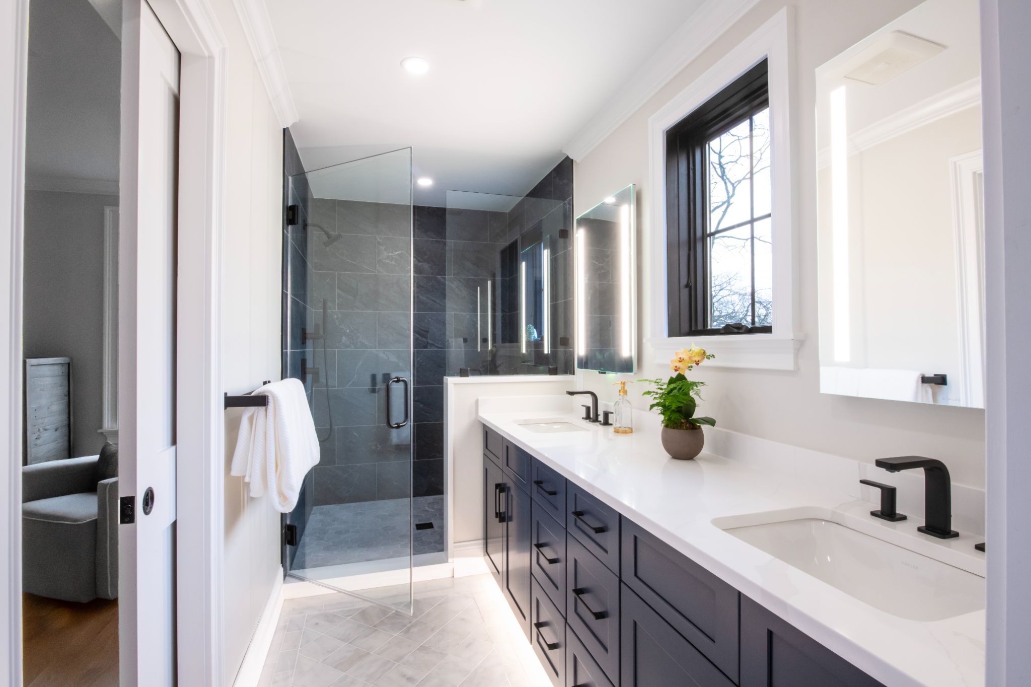 Modern bathroom with double sinks, dark cabinets, a glass-enclosed shower, large mirrors, and a window. White countertops and walls create a clean, bright atmosphere. Modern bathroom with double sinks, dark cabinets, a glass-enclosed shower, large mirrors, and a window. White countertops and walls create a clean, bright atmosphere.