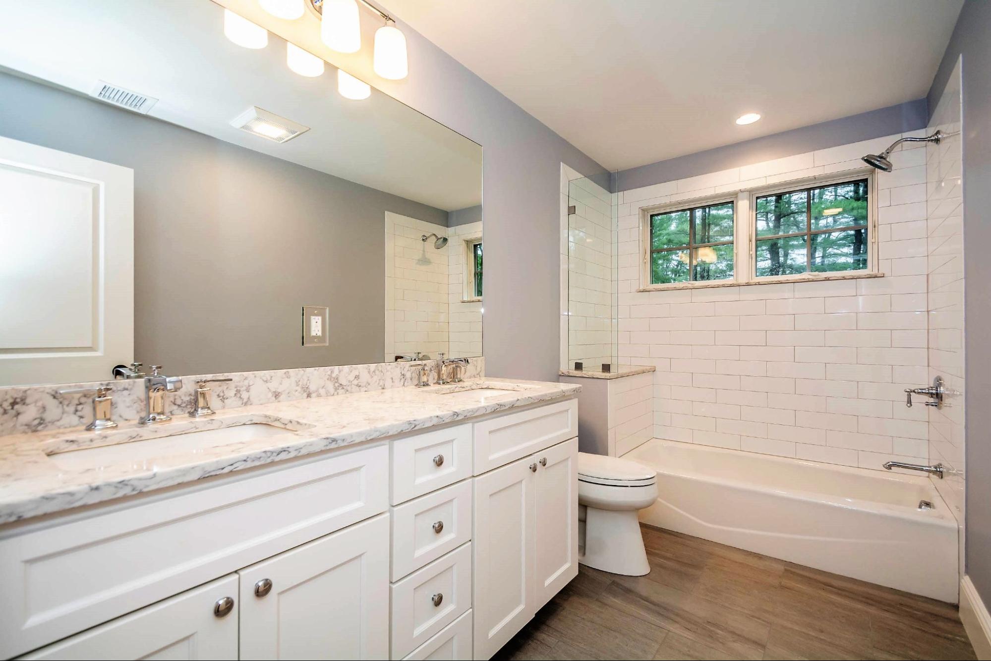 Bathroom with a double vanity, marble countertop, and a shower-tub combination with white subway tile walls.